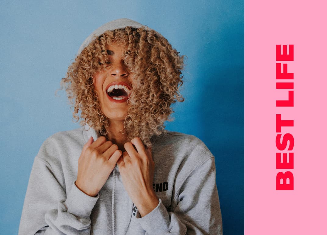 girl in grey hoodie laughing, eyes closed, hands resting on collar