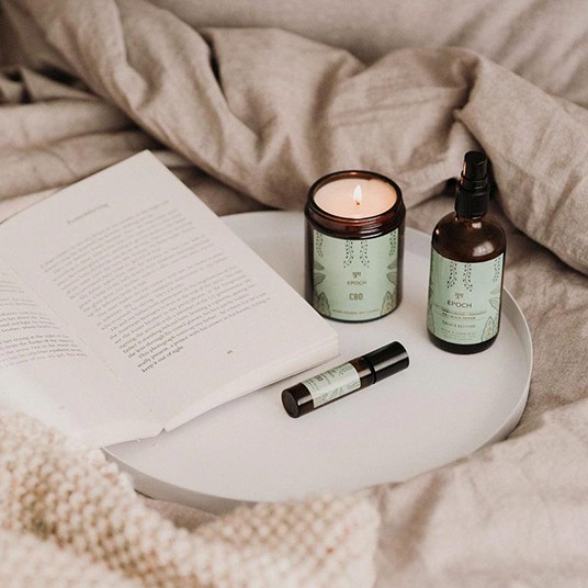 tray placed on bed with book, aromatherapy candle and two small bottles
