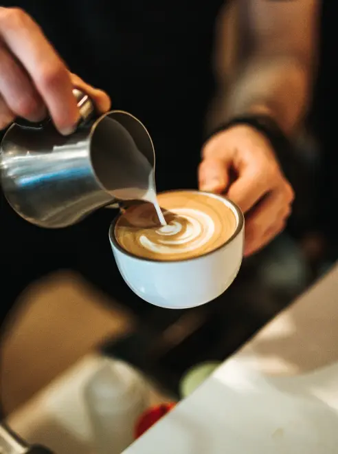 barista holding a cup pouring milk into coffee