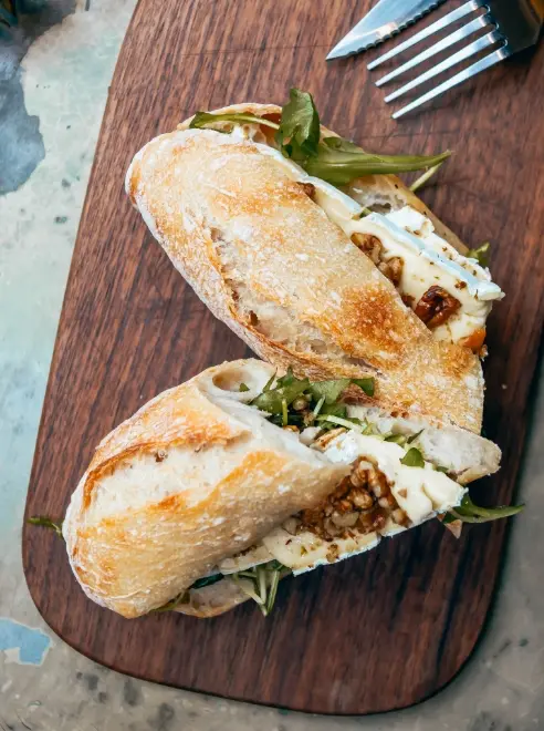 sandwich placed on a wooden board with knife and fork