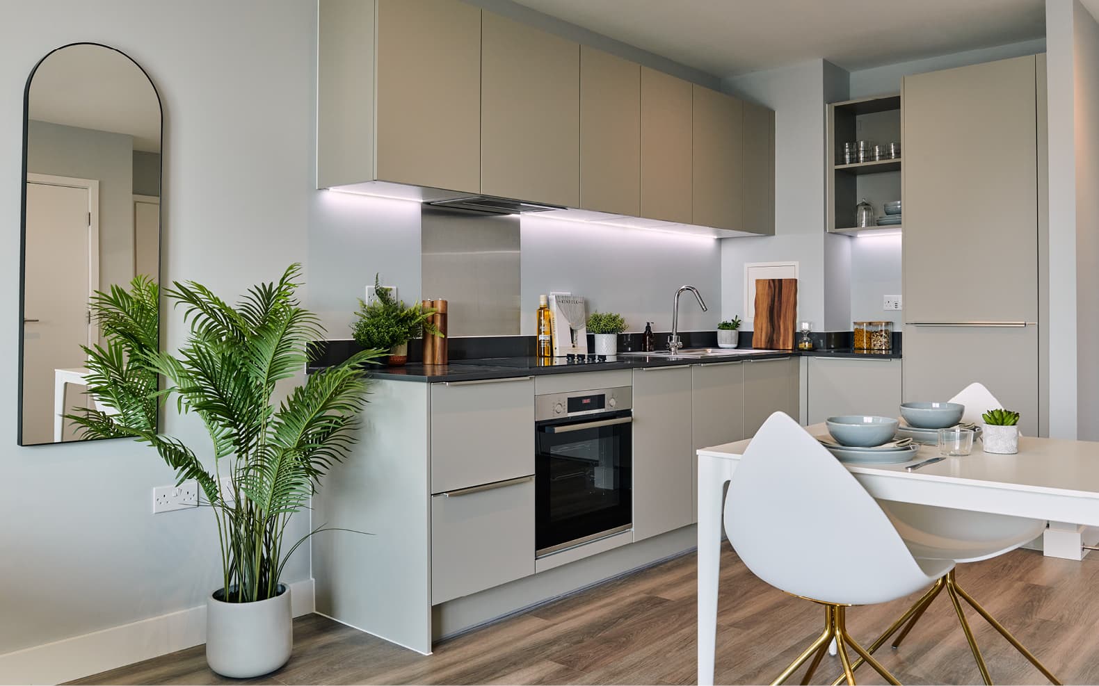 kitchen units with light under wall units, mirror on wall and plant in pot