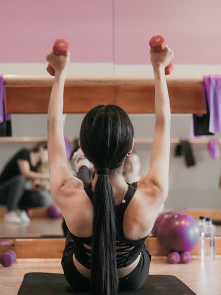 Person, viewed from behind in gym arms raised holding dumb bells