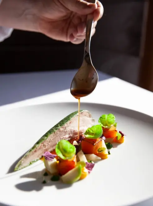 plate of fine dining food with sauce being drizzled over
