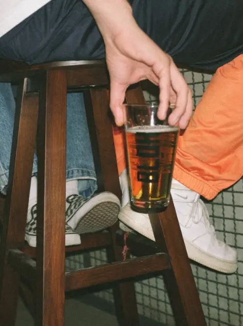 bottom half of person sat on bar stool holding a pint by his side